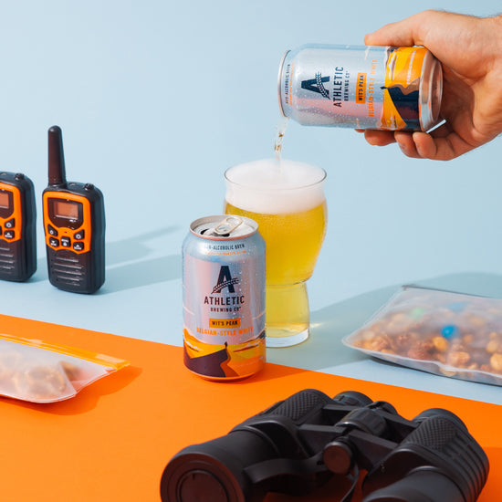 Person pouring Wit's Peak from a can into a glass with outdoor equipment on a colorful background