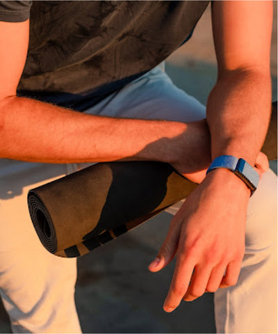 Blue Whoop band on wrist with yoga mat at sunset