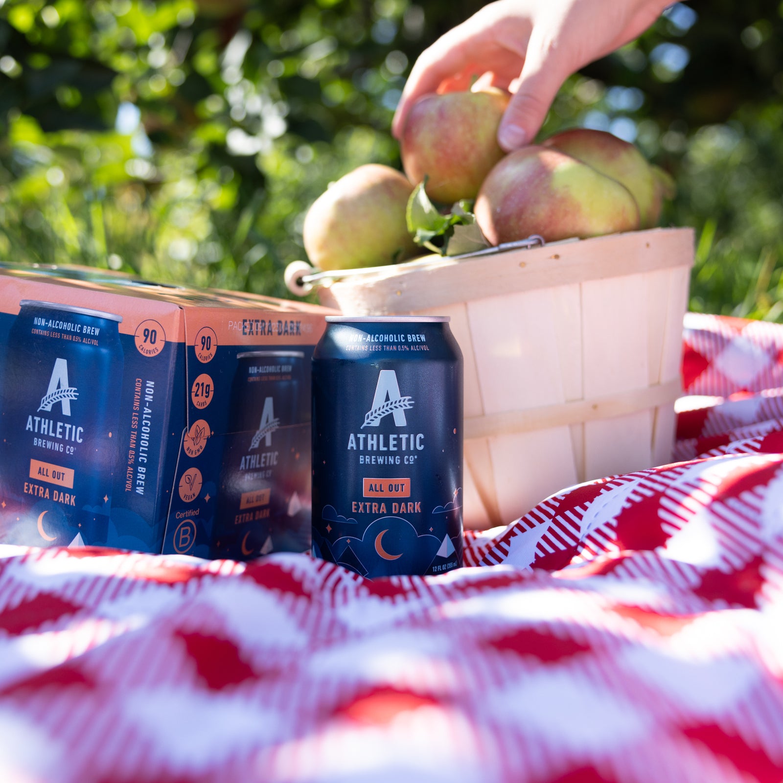 All Out cans on a picnic blanket next to apples