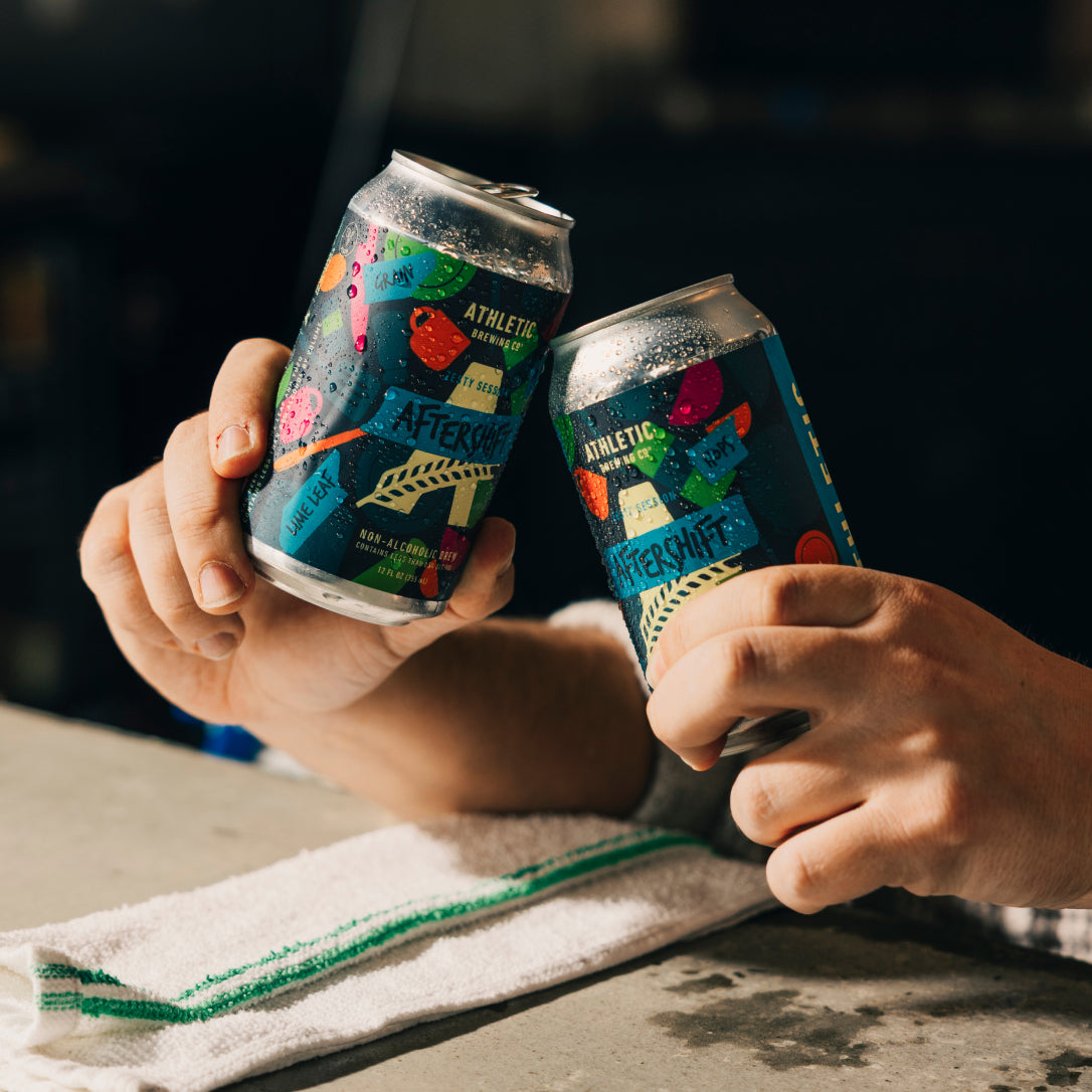 two Hands holding two cans of non-alcoholic brew with a white napkin