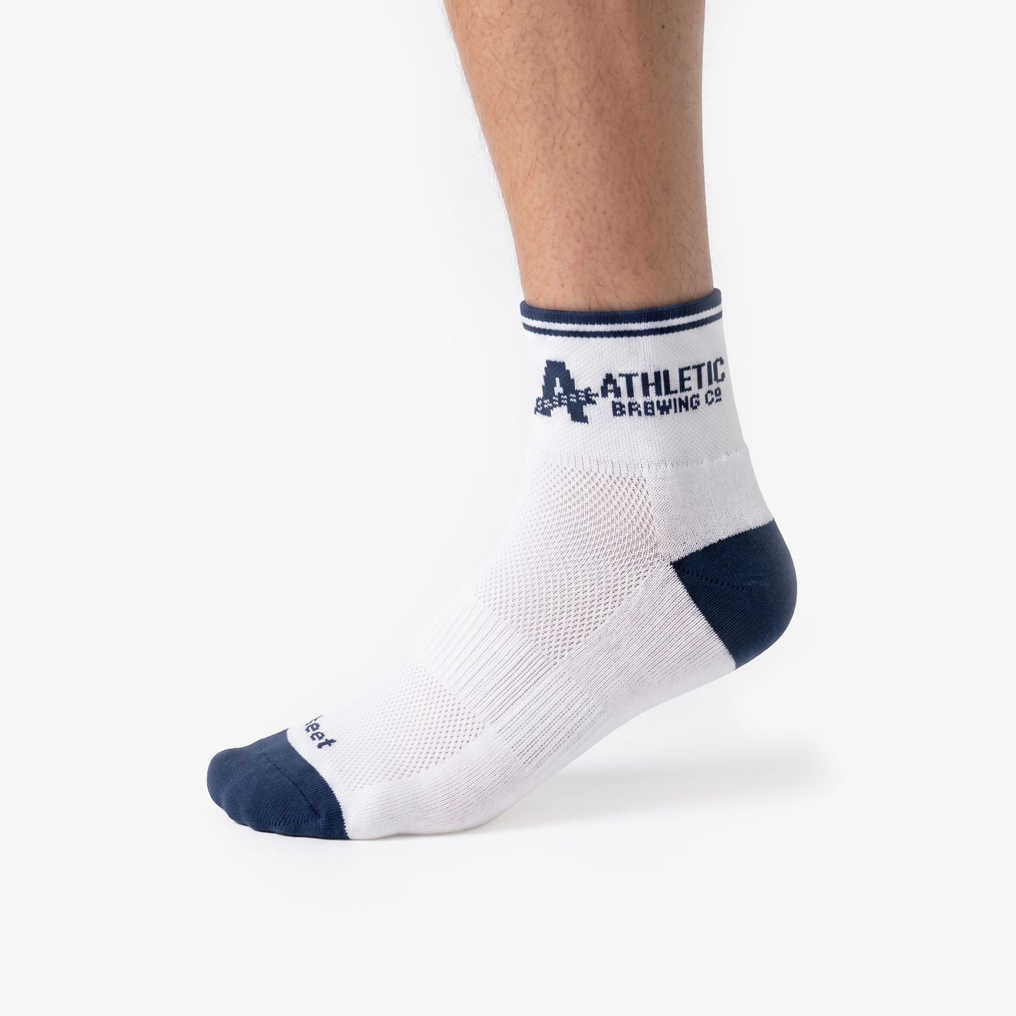 Person wearing white Athletic Brewing quarter crew performance socks with navy toe and heel accents, featuring striped cuffs and Athletic Brewing Co. logo branding near the ankle