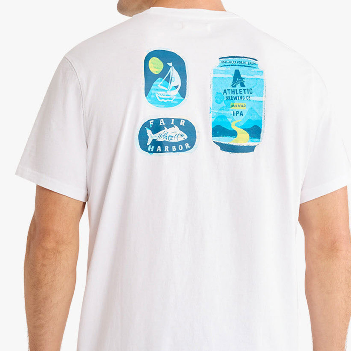 Back view of a white T-shirt featuring colorful graphic illustrations of a sailboat scene, a Fair Harbor fish logo, and an Athletic Brewing Co. Run Wild IPA can printed across the upper back.