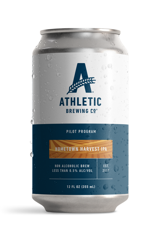 Athletic Brewing Company Pilot Program Hometown Harvest IPA 12 oz non-alcoholic beer can featuring a white and navy blue label with the Athletic Brewing logo and an orange harvest-inspired design. Contains less than 0.5% alcohol by volume.