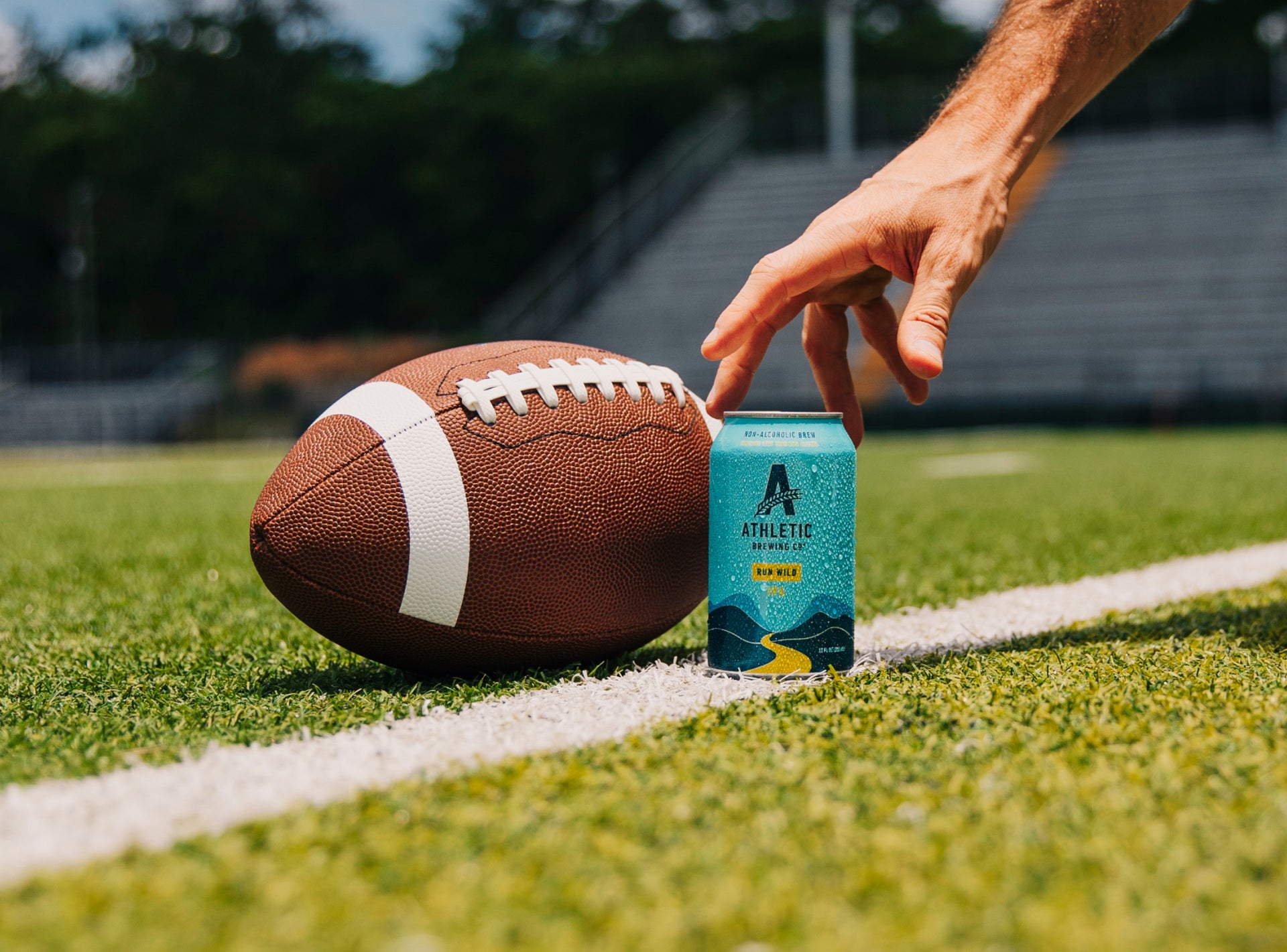 hand reaching for a can of Run Wild on a field next to a football