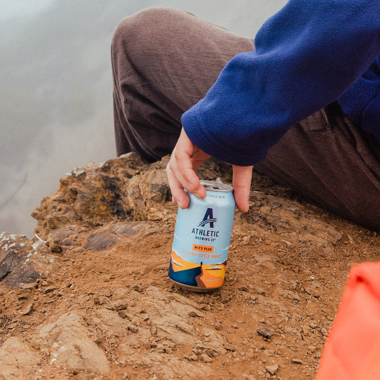 person on a cliff sitting with a can of Wit's Peak