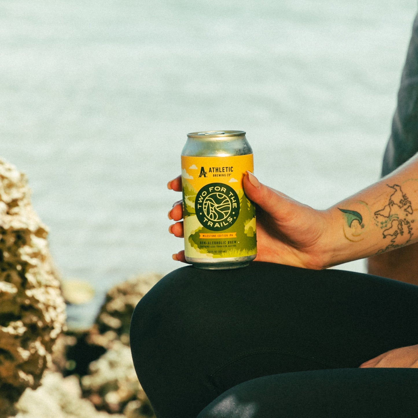 A close-up of a hand holding a condensation-covered can of Two for The Trails Milestone Edition IPA during a hike.