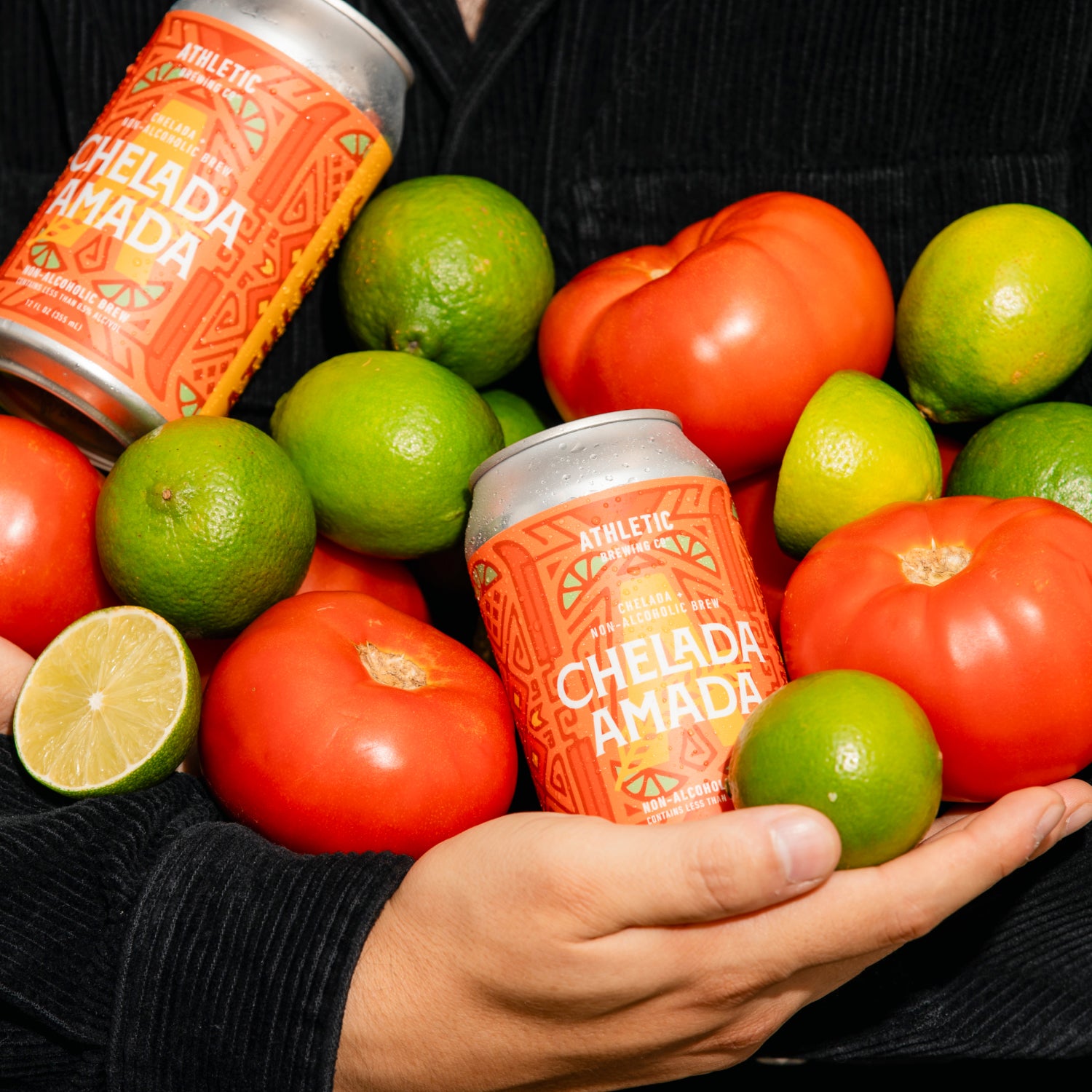 a person holding 2 cans of chelada amada limes and tomatos