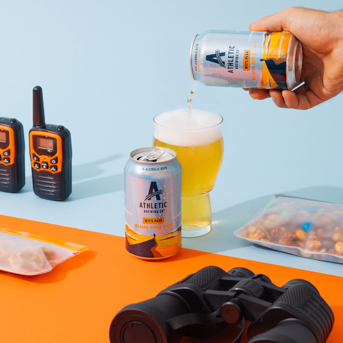 Person pouring Wit's Peak from a can into a glass with outdoor equipment on a colorful background