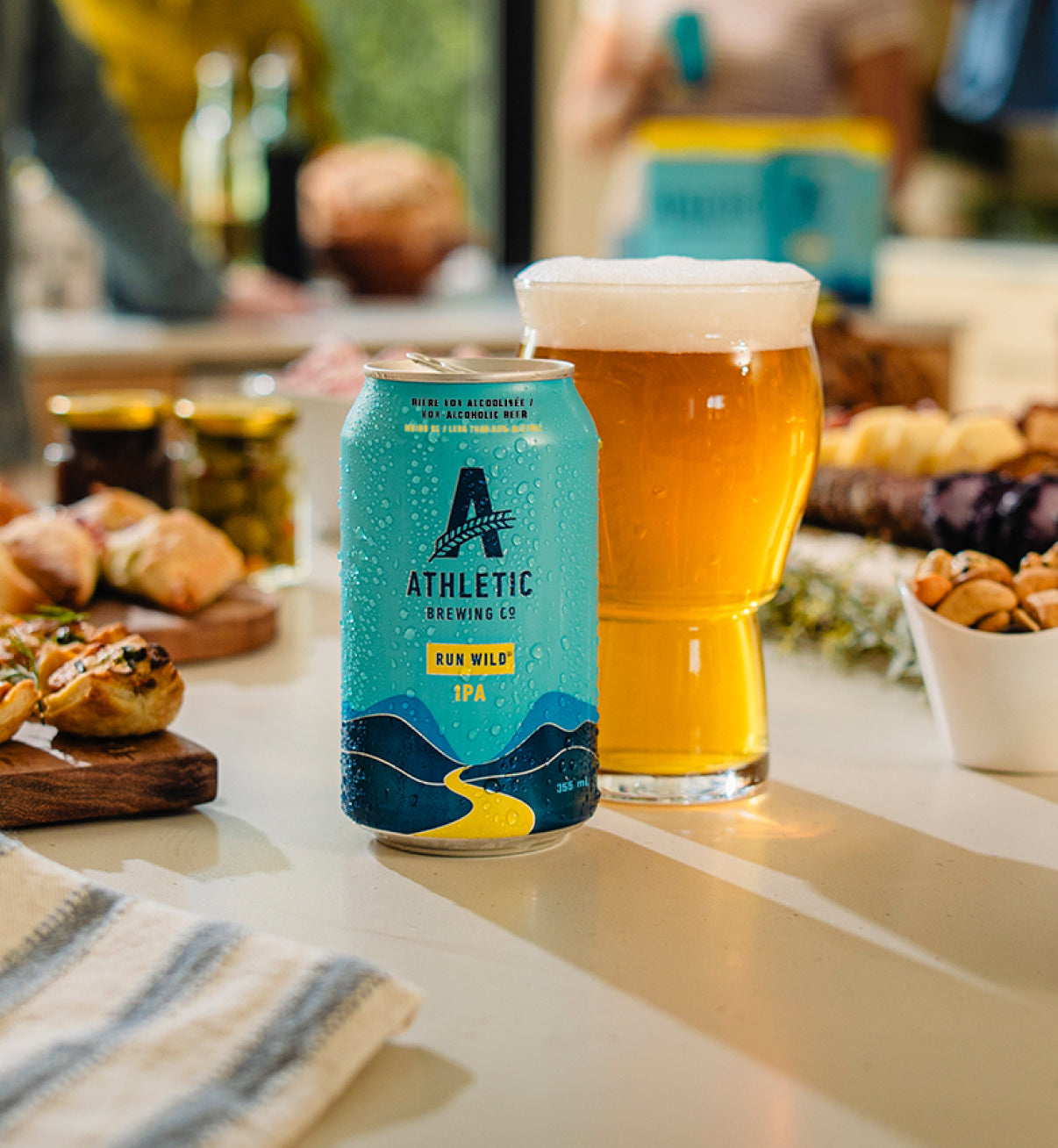glass and can of Athletic NA beer on table with food